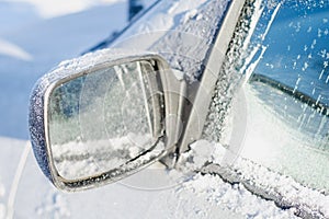 Car rearview mirror covered with white frost and snow on a sunny winter day