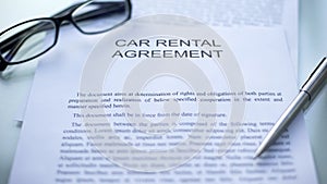 Car rental agreement lying on table, pen and eyeglasses on official document