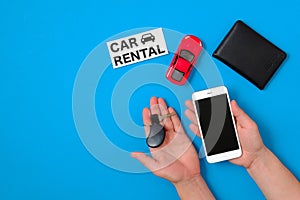 Car rental app concept. Toy car, auto drive license, human hand with smartphone and car key, text sign