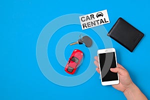 Car rental app concept. Toy car, car key, auto drive license, human hand with smartphone and text sign