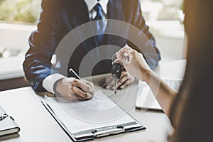 Car rental service concept. Close up view Hand of agent giving car key to customer after signed rental contract form