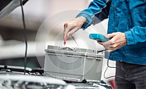 Car repaid garage technician checks lifespan of a car batery with a multimeter