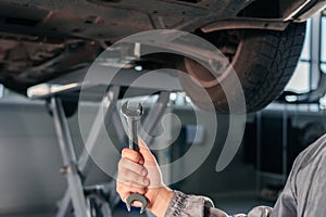 Car repair, maintenance and vehicle inspection concept. Man holding wrench in front of a car