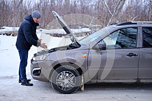 Car repair on the road in winter. a young man is trying to fix a car breakdown under the soot on the road. woodsroadside