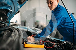 Car repairman with multimeter, battery inspection