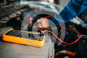 Car repairman with multimeter, battery inspection