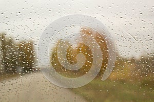 The car rides along the autumn road with rain drops on the windshield car window