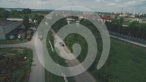 Car rides on the road out of town aerial view. Cars ride by road near fenced construction site at spring sunny day