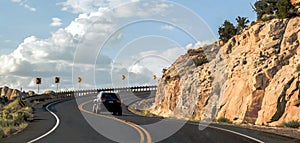 Car riding on a curvy road hairpin turn on a high terrace around a mountain with a scenic blue sky panorama