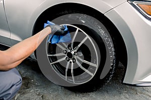 Car rims cleaning, car detailing wash concept. Cropped close up photo of male hand in black rubber glove with blue