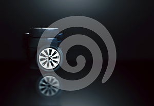 Car rims with tires and tire stacks with reflection, black background with white lights shining down