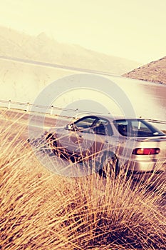 Car On The Road With Lake And Mountain Beyond It