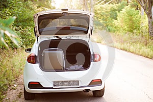 Car on the road with a suitcase in the trunk, travel concept. White cars parked on the roadside, with natural