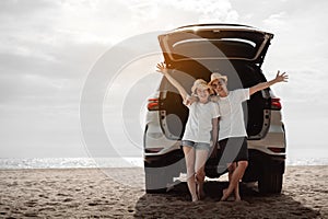 Car road trip travel of couple enjoying beach relaxing on hood of sports utility car. Happy Asian woman, man friends smiling