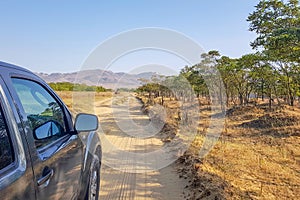 The car is on the road of white sand. Near the road green plants. Blue sky and mountains in the background. Dagestan, Russian