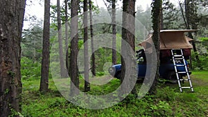 A car roof top tent for camping on the roof rack of an off-road car in a forest on a misty cloudy morning.