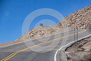 Car rounding sharp bend with steep dropoff on dangerous mountain road with blue sky behind