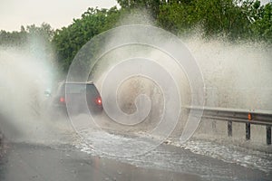 Car runs into big puddle at heavy rain, water splashing over the car. Car driving on asphalt road at thunder storm. Dangerous