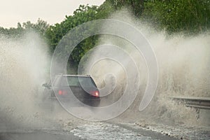 Car runs into big puddle at heavy rain, water splashing over the car. Car driving on asphalt road at thunder storm. Dangerous