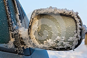 The car`s rearview mirror is covered in frost and snow. Icing of transport and unfavorable conditions for traffic