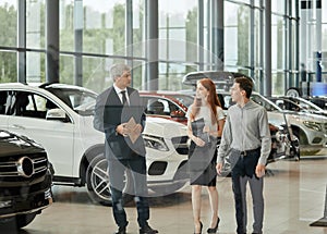Car sales manager telling about the features of the car to the customers at the dealership
