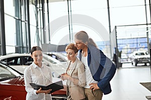 Car sales manager telling about the features of the car to the customers at the dealership