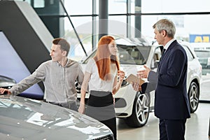 Car sales manager telling about the features of the car to the customers at the dealership