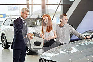 Car sales manager telling about the features of the car to the customers at the dealership