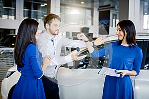 Car salesgirl giving the key of the new car to the attractive couple owners.