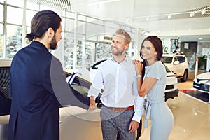 A car salesman and a buyer shake hands. A couple buys a car