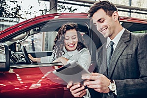 Car salesman giving explanations on tablet to pretty young woman