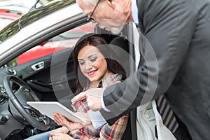 Car salesman giving explanations on tablet to young woman