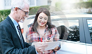 Car salesman giving explanations on tablet to young woman