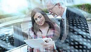 Car salesman giving explanations on tablet to young woman, light