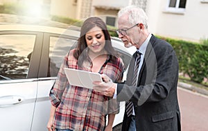 Car salesman giving explanations on tablet to young woman, light effect