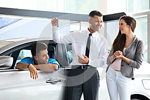 Car Salesman Giving a Key From the New Car to the Young Owners