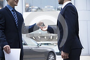 Car salesman handing over the keys for a new car to a young businessman