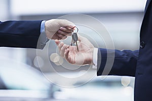 Car salesman handing over the keys for a new car to a young businessman, close-up