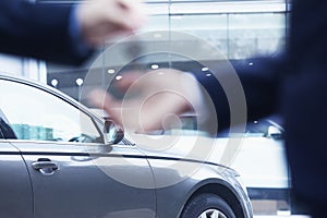 Car salesman handing over the keys for a new car to a young businessman, close-up