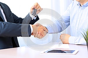 Car salesman handing over the keys for a new car to a young businessman . Handshake between two business people.