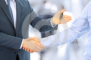 Car salesman handing over the keys for a new car to a young businessman . Handshake between two business people. Focus on a key