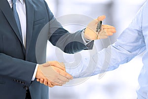 Car salesman handing over the keys for a new car to a young businessman . Handshake between two business people. Focus on a key