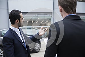 Car salesman holding car keys and selling a car to a young businessman