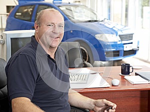 Car salesman sitting in showroom smiling