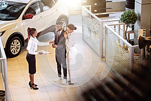 Car salesman standing at dealership telling about features of car to customers