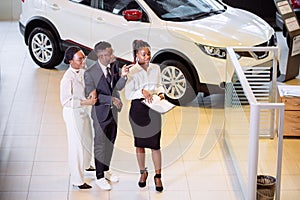 Car salesman standing at dealership telling about features of car to customers