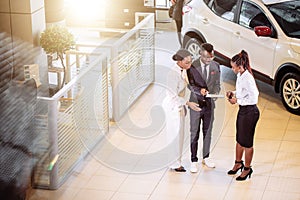 Car salesman standing at dealership telling about features of car to customers