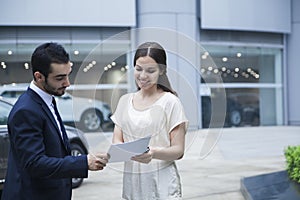 Car salesman and young woman looking over the paperwork at a car dealership