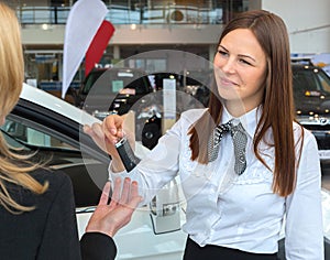 Car saleswoman handing over keys for a new car to young woman