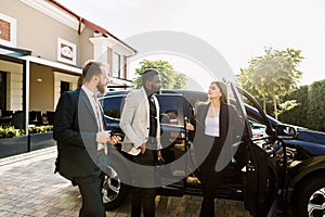 Car salon, sale and rent concept. African and Caucasian men in business wear buying the car. Elegant woman car